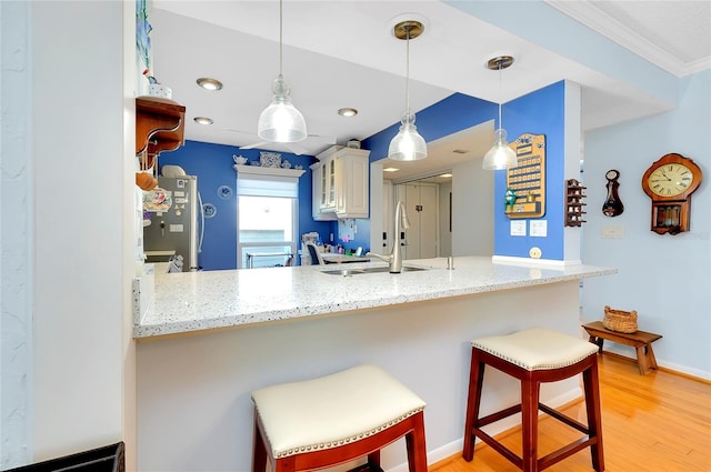 kitchen with pendant lighting, a sink, a kitchen breakfast bar, freestanding refrigerator, and light wood-style floors