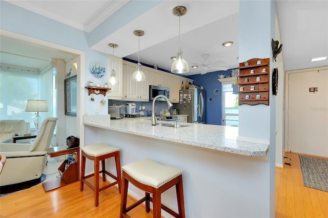 kitchen featuring a peninsula, a sink, appliances with stainless steel finishes, a kitchen breakfast bar, and backsplash