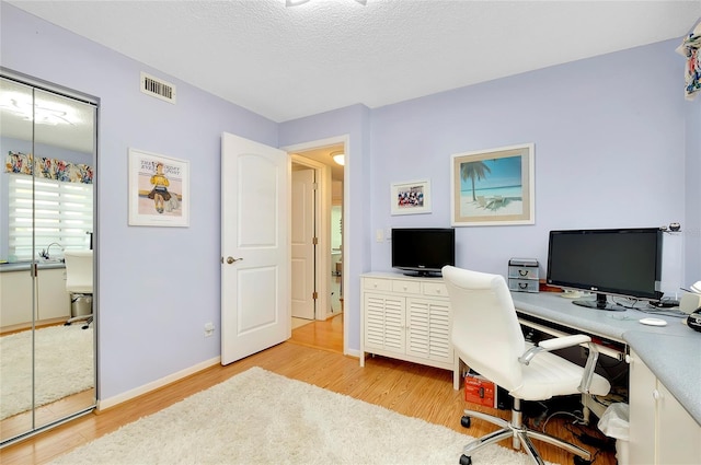 office with visible vents, light wood-style flooring, a textured ceiling, and baseboards