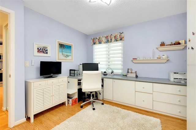 office area with light wood-style flooring, a textured ceiling, and baseboards