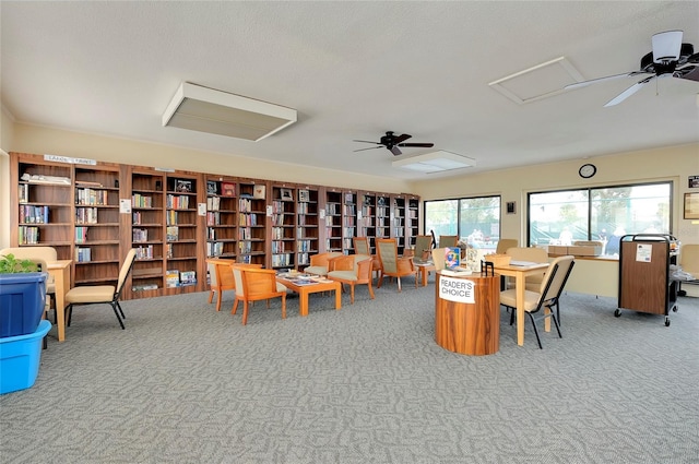 carpeted office with attic access, ceiling fan, and wall of books