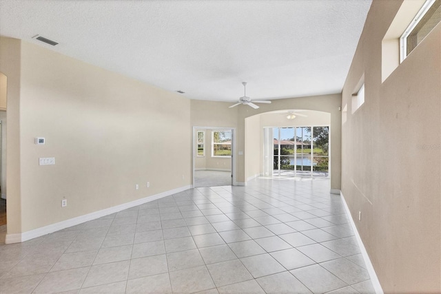 spare room with light tile patterned floors, a textured ceiling, arched walkways, and visible vents