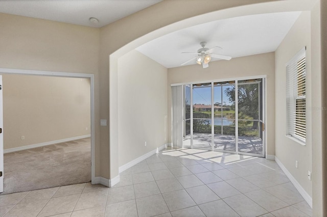 spare room with light tile patterned floors, arched walkways, baseboards, light colored carpet, and ceiling fan