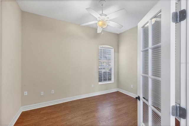 empty room with dark wood-type flooring, a ceiling fan, and baseboards