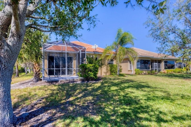 rear view of house with a lanai, a lawn, a tiled roof, and stucco siding