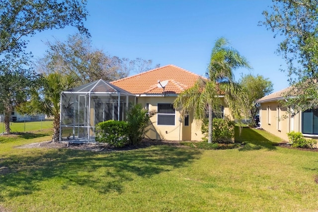 rear view of property with a lanai, a tile roof, a lawn, and stucco siding