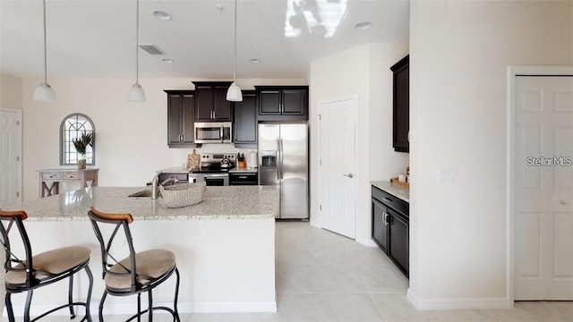 kitchen featuring decorative light fixtures, appliances with stainless steel finishes, light stone countertops, and a kitchen breakfast bar