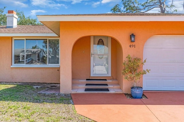 doorway to property with a garage, roof with shingles, a chimney, and stucco siding