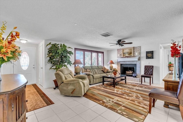 living area with a fireplace, light tile patterned floors, visible vents, ceiling fan, and a textured ceiling