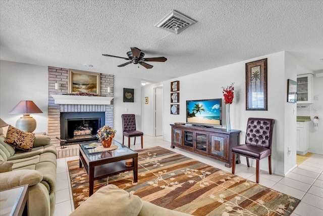 living area featuring visible vents, a ceiling fan, a brick fireplace, light tile patterned flooring, and a textured ceiling