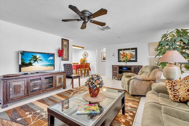 living room featuring light tile patterned floors, a textured ceiling, visible vents, and a ceiling fan