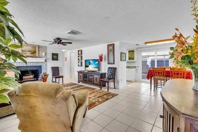 living area featuring visible vents, ceiling fan, a textured ceiling, a fireplace, and light tile patterned flooring