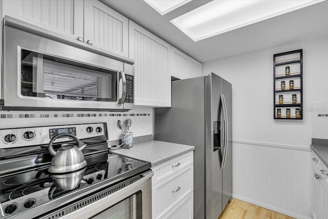 kitchen featuring a wainscoted wall, appliances with stainless steel finishes, light countertops, light wood-style floors, and white cabinetry