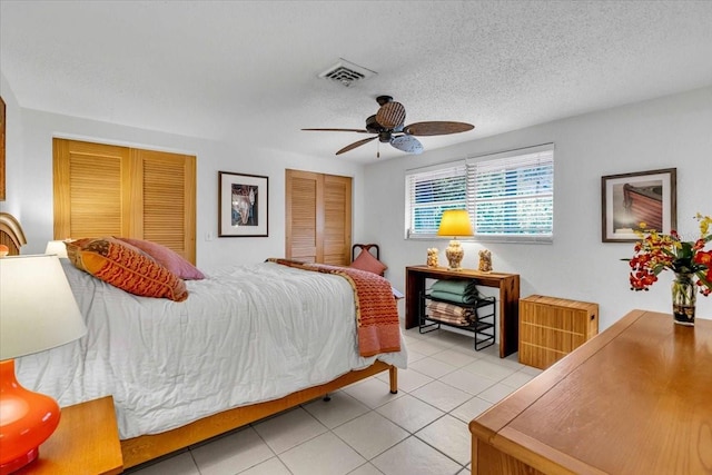 tiled bedroom with a textured ceiling, ceiling fan, visible vents, and multiple closets