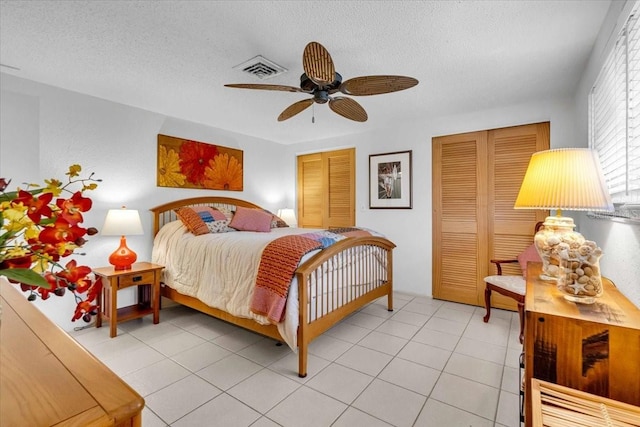 bedroom featuring light tile patterned floors, visible vents, ceiling fan, a textured ceiling, and multiple closets