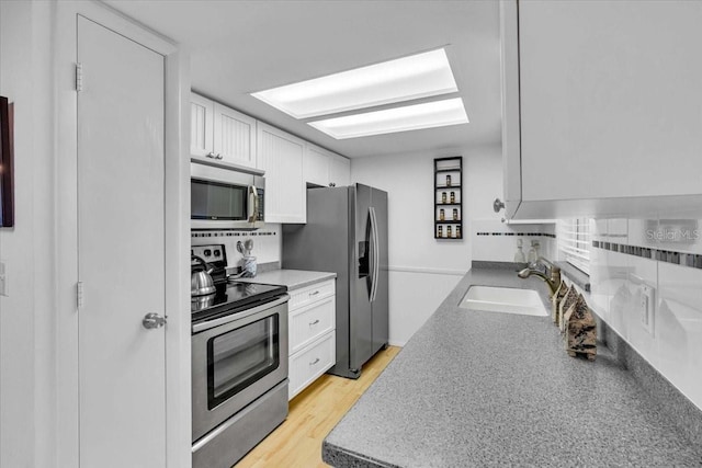 kitchen with stainless steel appliances, light wood-type flooring, white cabinetry, and a sink