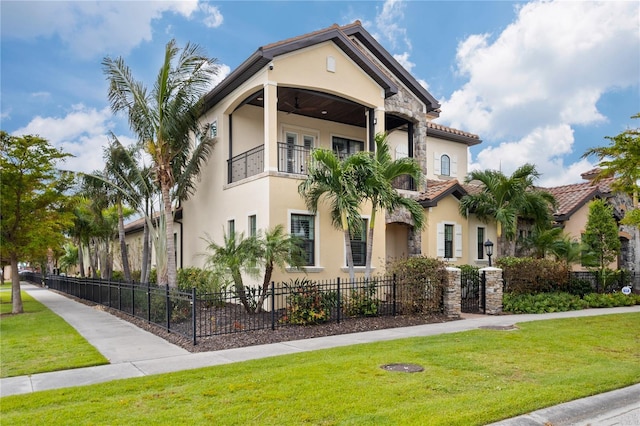 mediterranean / spanish home featuring a balcony, a fenced front yard, a front lawn, and stucco siding