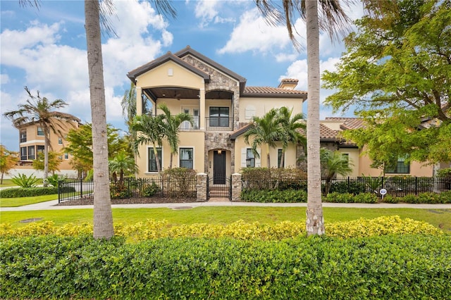 mediterranean / spanish house featuring a balcony, stone siding, a fenced front yard, and stucco siding