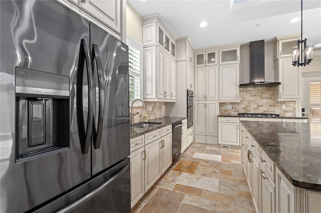 kitchen with stone tile flooring, fridge with ice dispenser, wall chimney range hood, a sink, and dishwasher