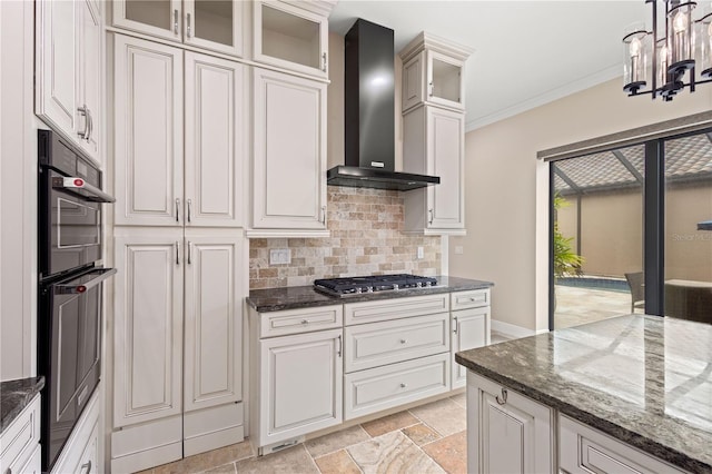 kitchen with wall chimney exhaust hood, ornamental molding, dark stone countertops, stainless steel gas stovetop, and backsplash