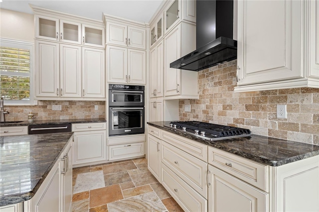 kitchen with stainless steel gas cooktop, stone tile floors, tasteful backsplash, dobule oven black, and wall chimney range hood