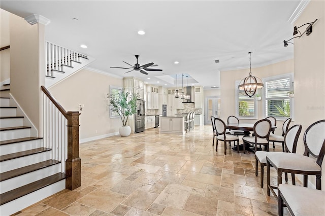 living area with stone tile floors, baseboards, ornamental molding, stairs, and ceiling fan with notable chandelier