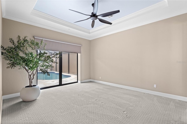 carpeted spare room with ornamental molding, a raised ceiling, ceiling fan, and baseboards