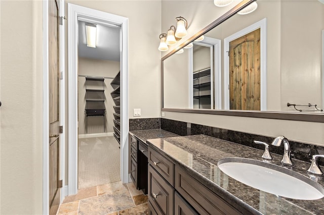 full bath with stone tile floors, a spacious closet, and vanity