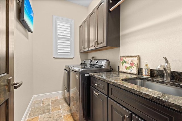 clothes washing area with cabinet space, stone tile floors, baseboards, separate washer and dryer, and a sink