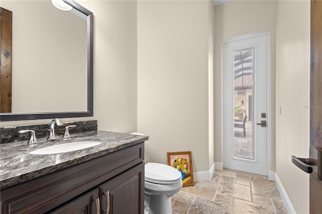 bathroom featuring stone tile flooring, toilet, vanity, and baseboards