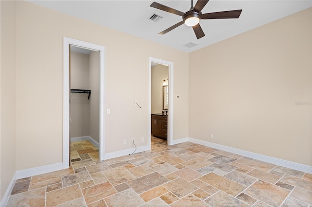 unfurnished bedroom featuring a walk in closet, stone tile flooring, visible vents, ensuite bath, and baseboards