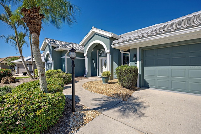 view of front of property featuring a garage, a tiled roof, driveway, and stucco siding