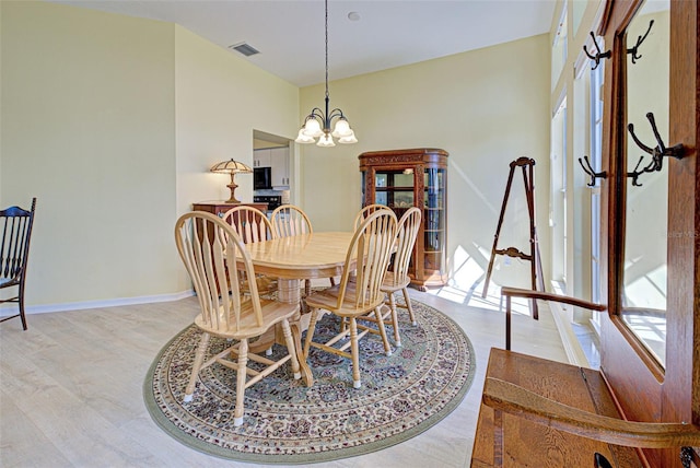 dining area with baseboards, visible vents, light wood finished floors, and an inviting chandelier