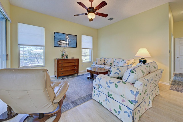 living area with light wood-style floors, visible vents, ceiling fan, and baseboards