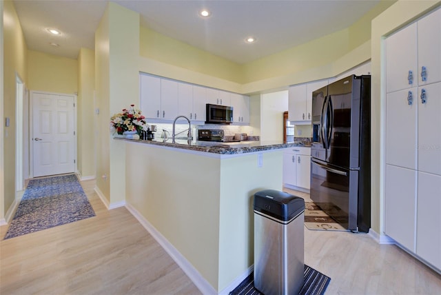 kitchen featuring stainless steel microwave, light wood-style floors, white cabinetry, a peninsula, and black fridge