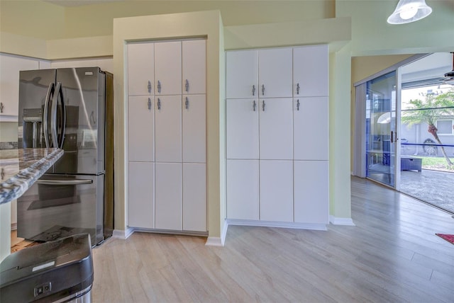 kitchen featuring light stone counters, stainless steel fridge, white cabinets, and light wood-style floors