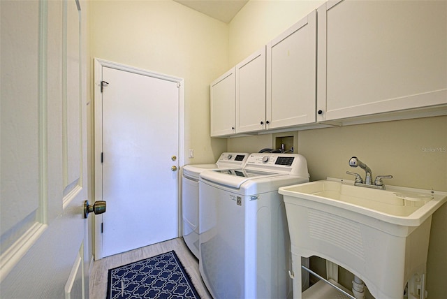 washroom with light wood-type flooring, cabinet space, a sink, and washing machine and clothes dryer