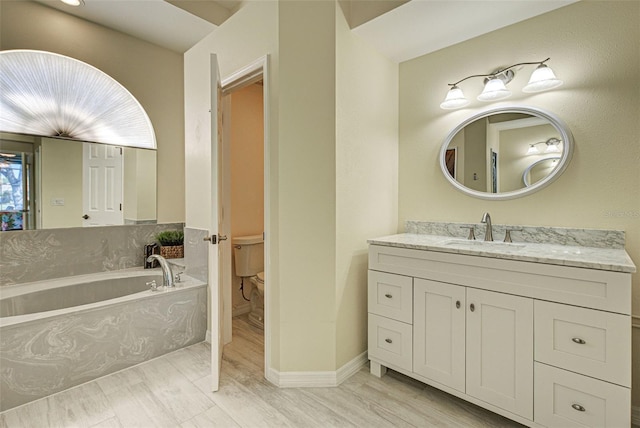 bathroom with a garden tub, vanity, toilet, and wood finished floors