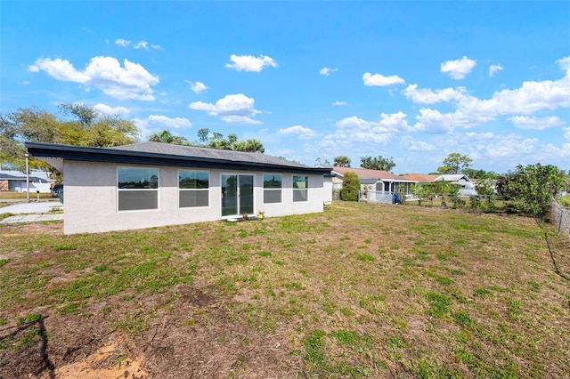 rear view of property featuring a yard, fence, and stucco siding