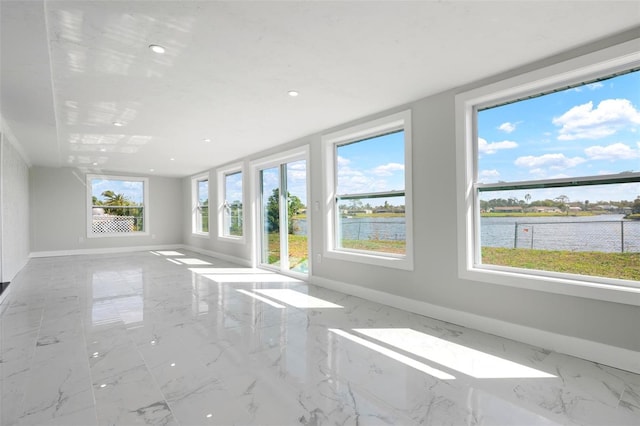 unfurnished living room with recessed lighting, baseboards, marble finish floor, and a water view