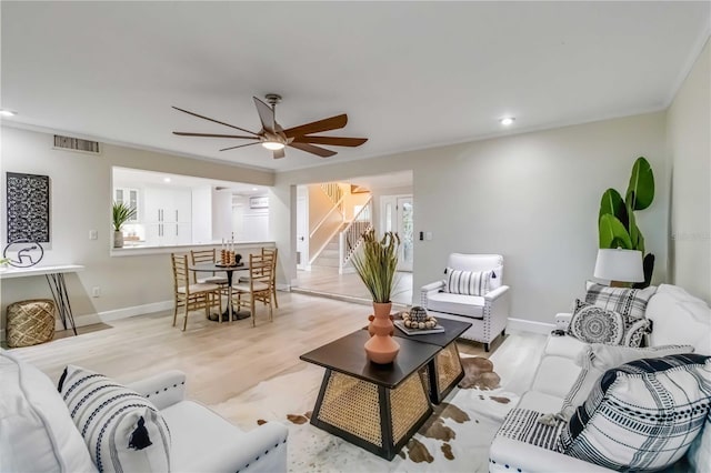 living area with light wood-type flooring, visible vents, a ceiling fan, stairway, and baseboards