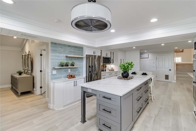 kitchen with a breakfast bar, gray cabinets, stainless steel appliances, and light wood-style flooring