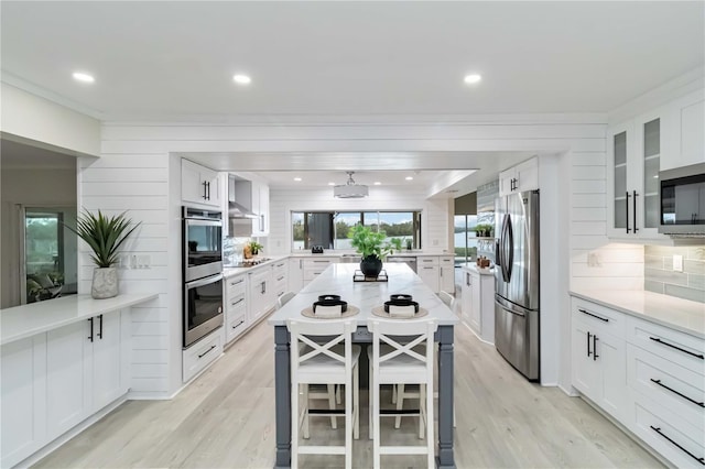 kitchen featuring stainless steel appliances, backsplash, light wood-style flooring, and white cabinetry