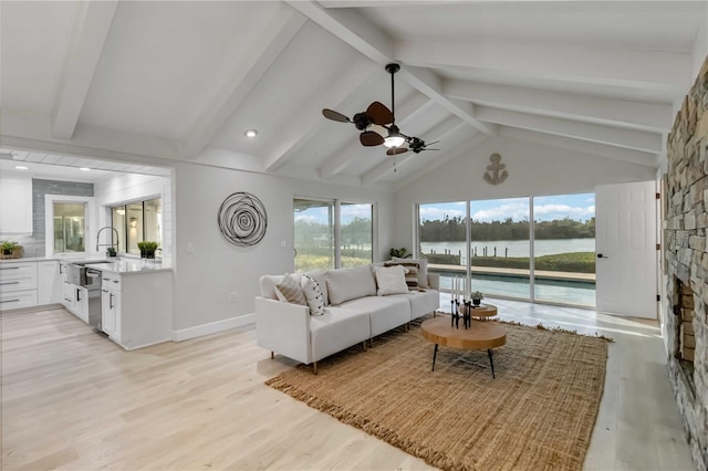 living room featuring baseboards, vaulted ceiling with beams, ceiling fan, light wood-style floors, and a water view