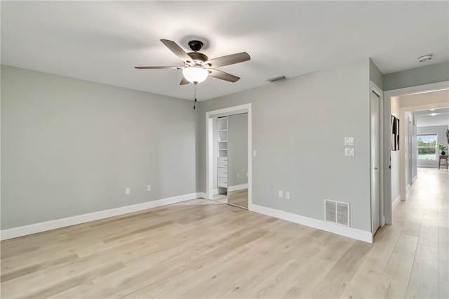 empty room featuring light wood-style flooring, a ceiling fan, visible vents, and baseboards