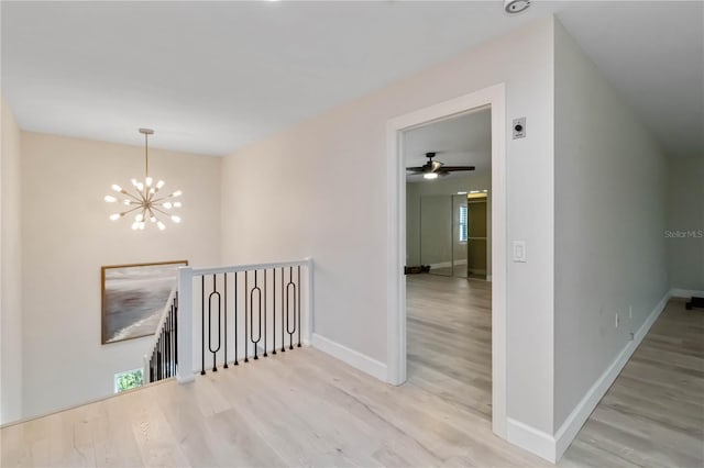 hall with wood finished floors, an upstairs landing, and a chandelier