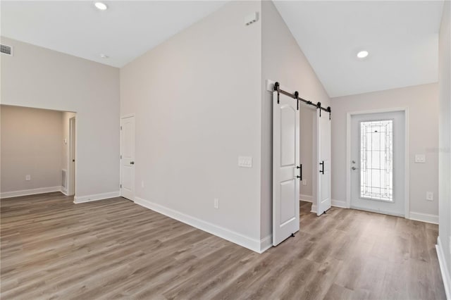 interior space with light wood-type flooring, a barn door, baseboards, and vaulted ceiling