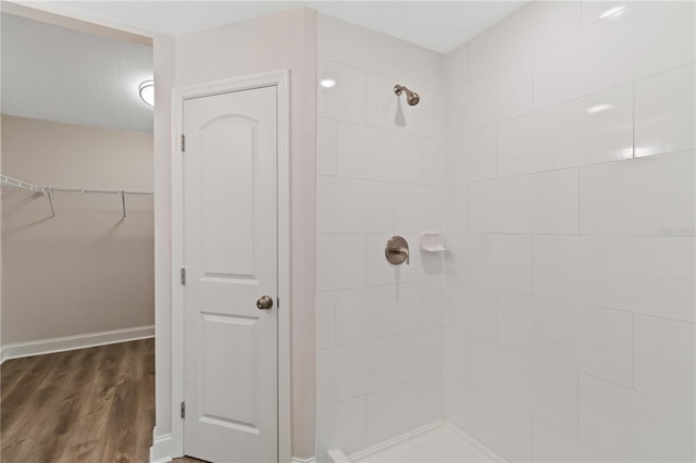 full bath featuring a walk in closet, wood finished floors, baseboards, and tiled shower