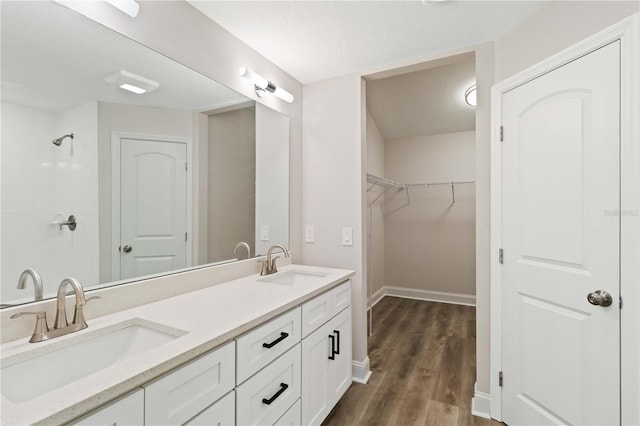 full bath with double vanity, wood finished floors, baseboards, and a sink