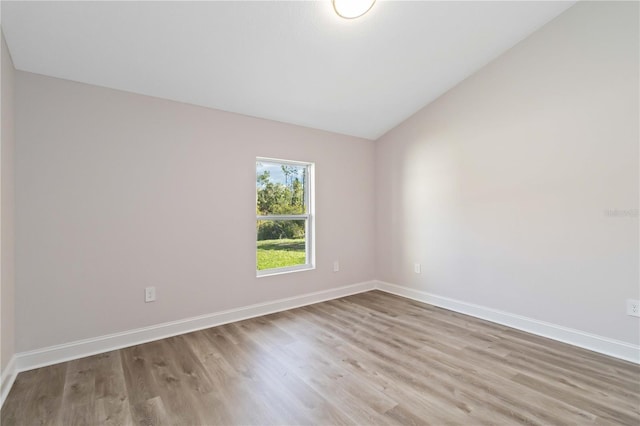 spare room featuring baseboards, lofted ceiling, and wood finished floors